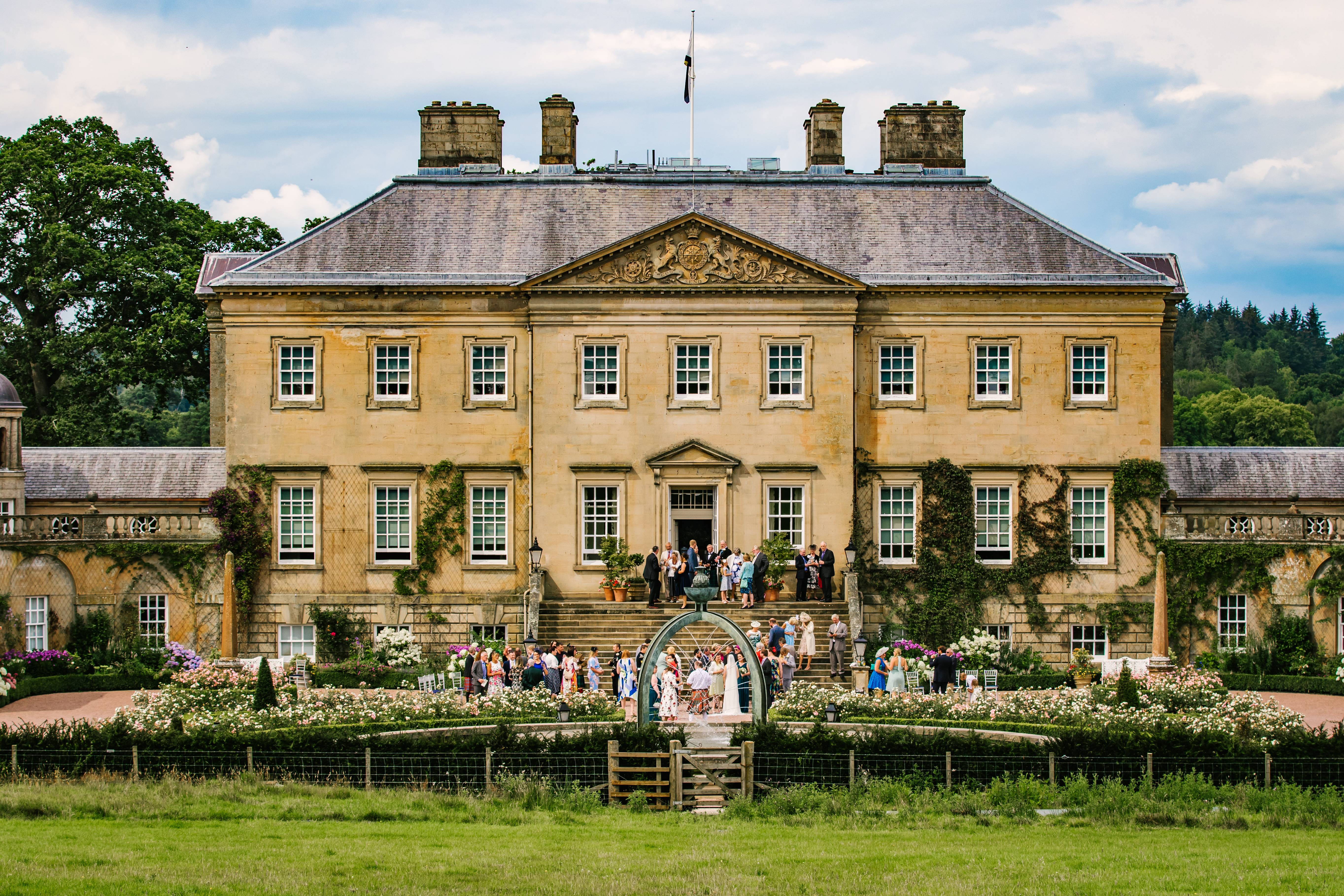 Anna & David — grand stately home with wedding guests gathered on the steps and rose garden